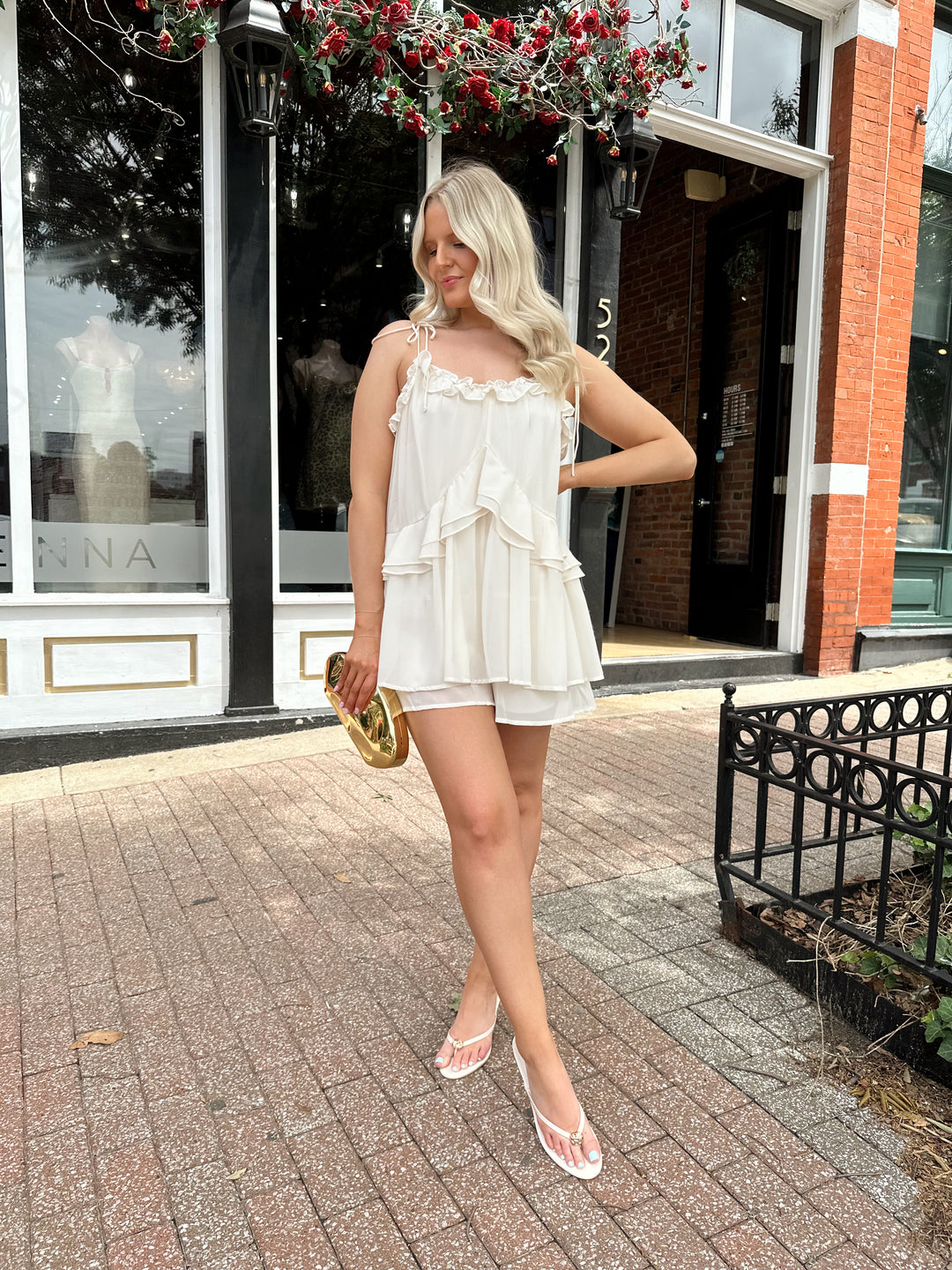 Woman wearing ivory colored romper with ruffle tiered detailing, and self tie straps.