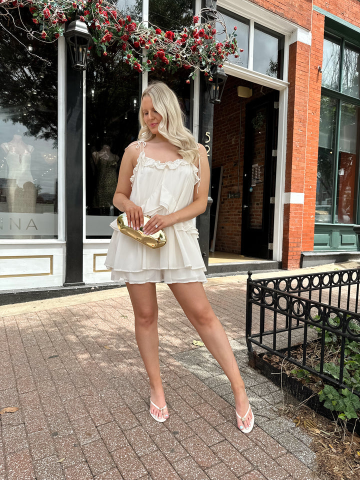 Woman wearing ivory colored romper with ruffle tiered detailing, and self tie straps.