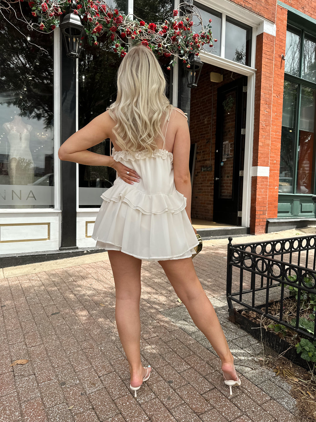 Woman wearing ivory colored romper with ruffle tiered detailing, and self tie straps.