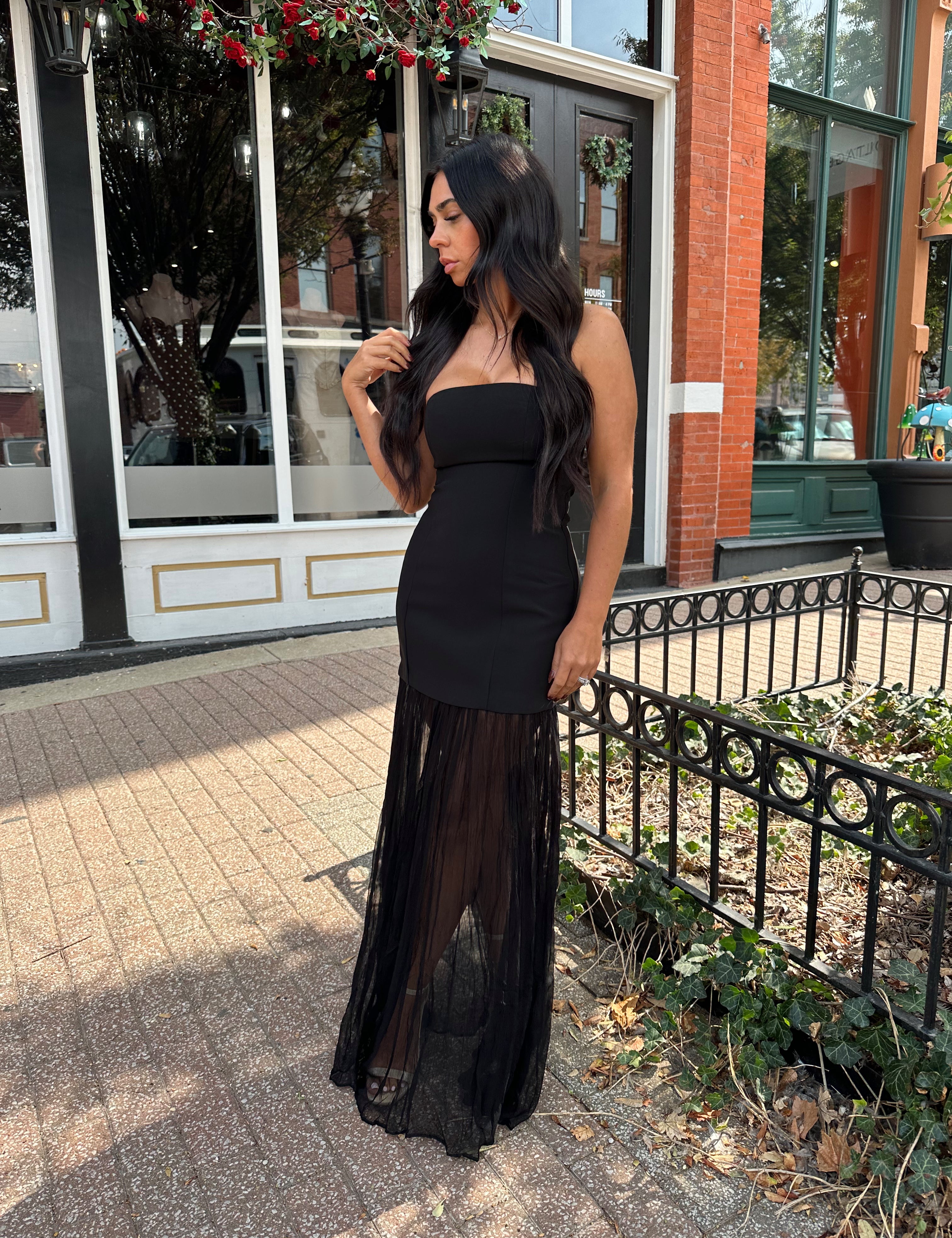 Woman wearing black strapless maxi dress with sheer overlay bottom.