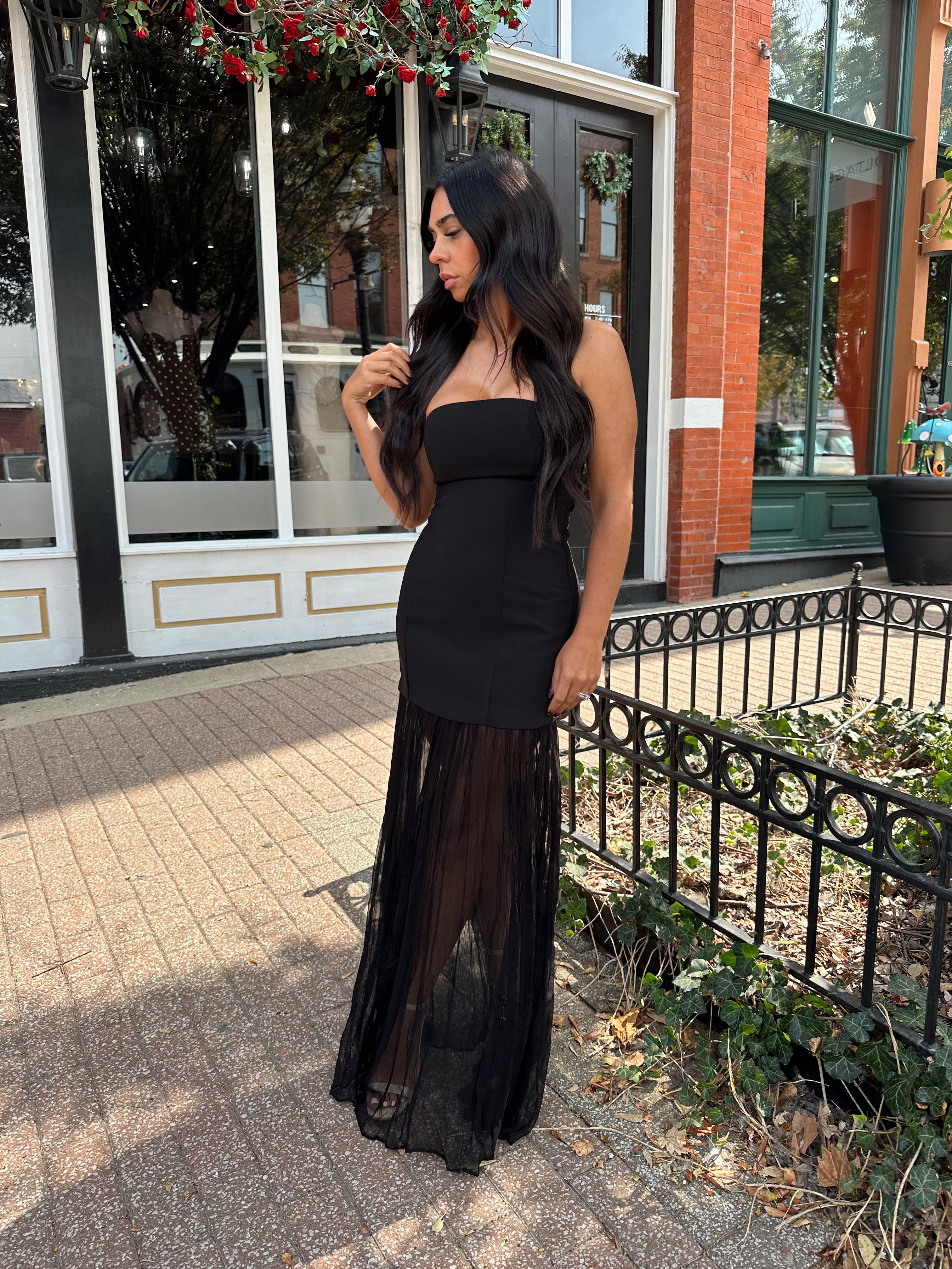 Woman wearing black strapless maxi dress with sheer overlay bottom.