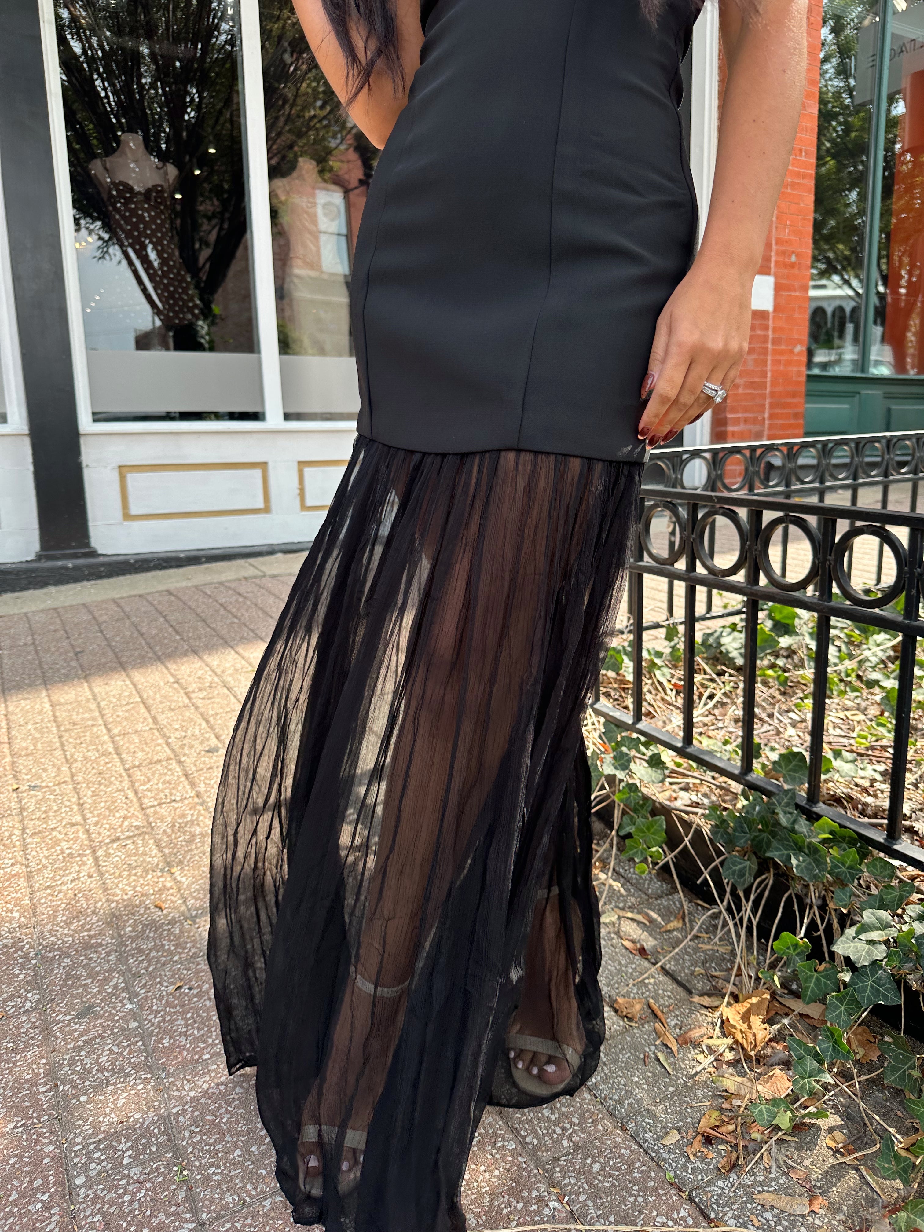 Woman wearing black strapless maxi dress with sheer overlay bottom.