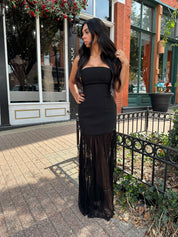 Woman wearing black strapless maxi dress with sheer overlay bottom.