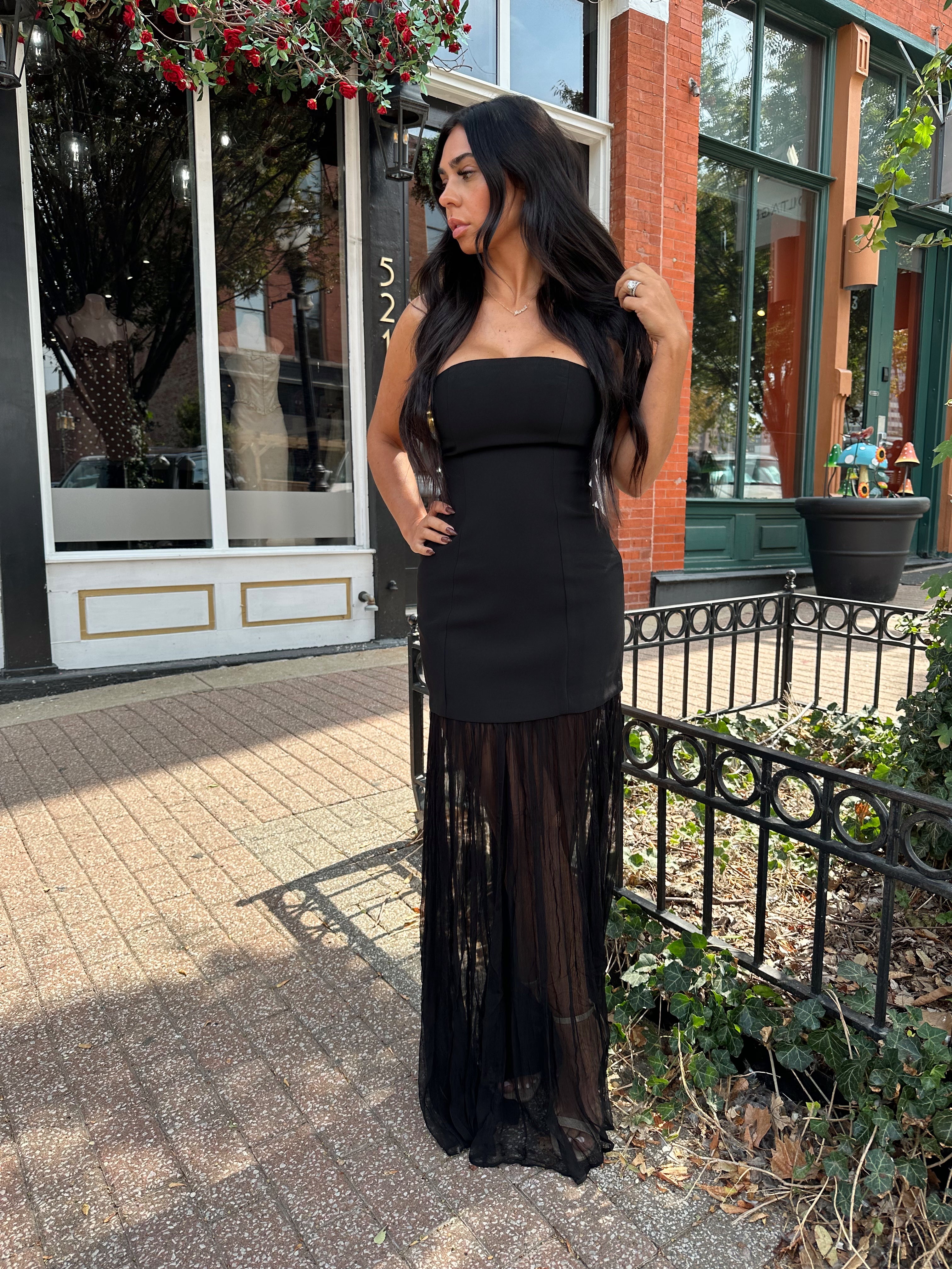 Woman wearing black strapless maxi dress with sheer overlay bottom.