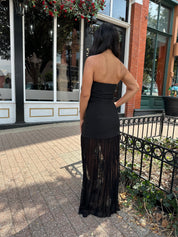 Woman wearing black strapless maxi dress with sheer overlay bottom.