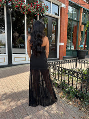 Woman wearing black strapless maxi dress with sheer overlay bottom.