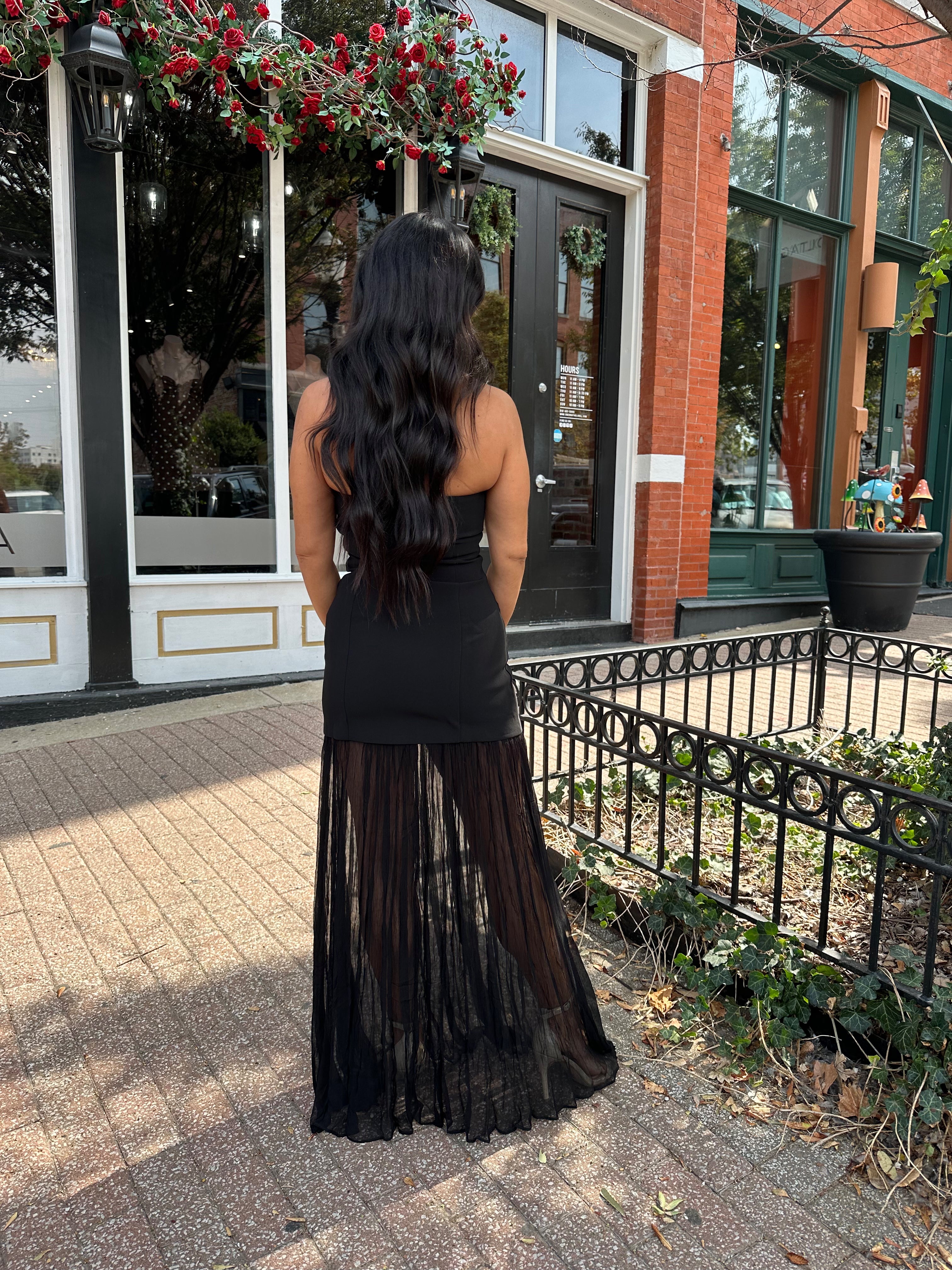 Woman wearing black strapless maxi dress with sheer overlay bottom.