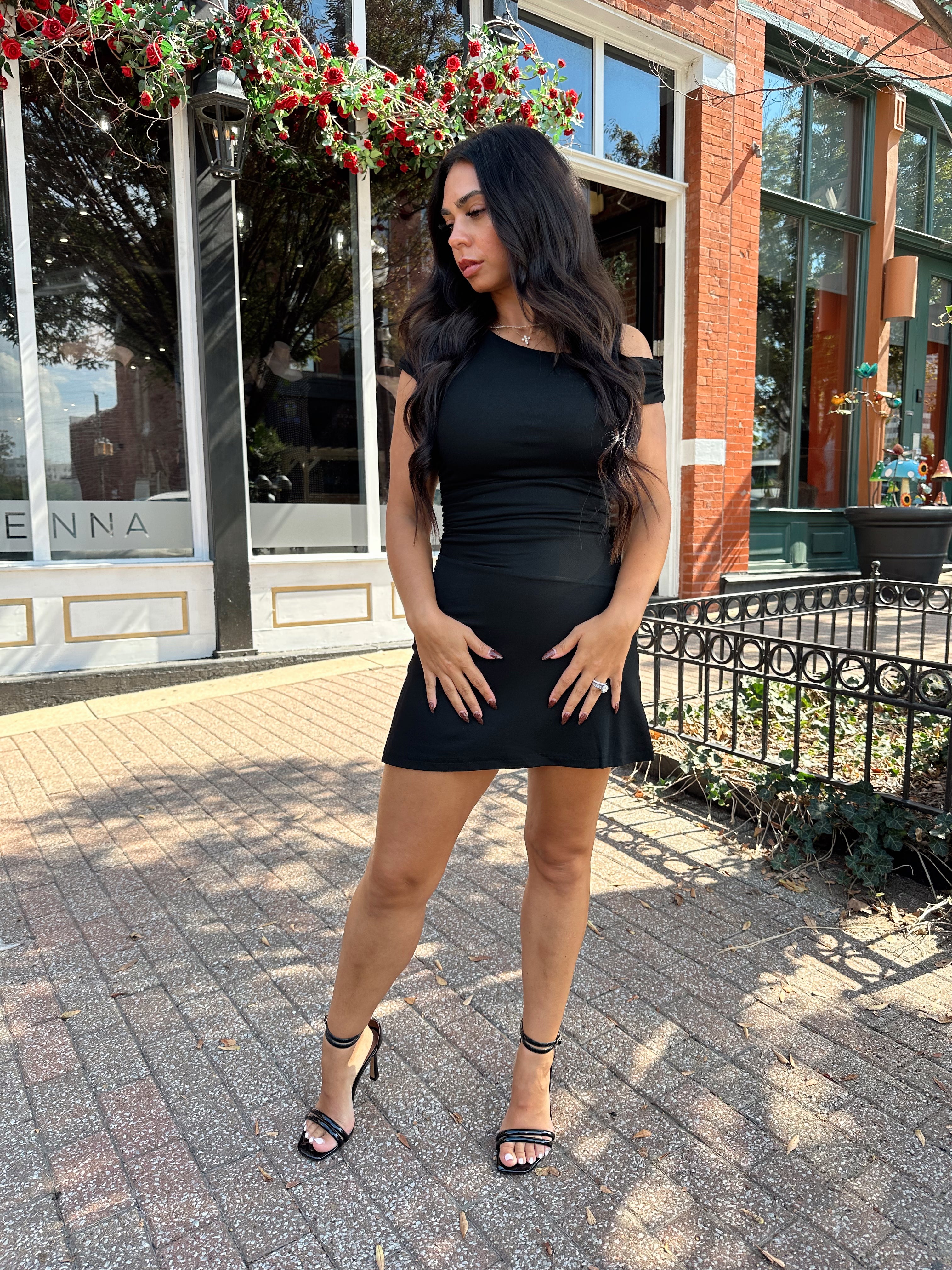Woman wearing black asymmetrical mini dress with black heels.