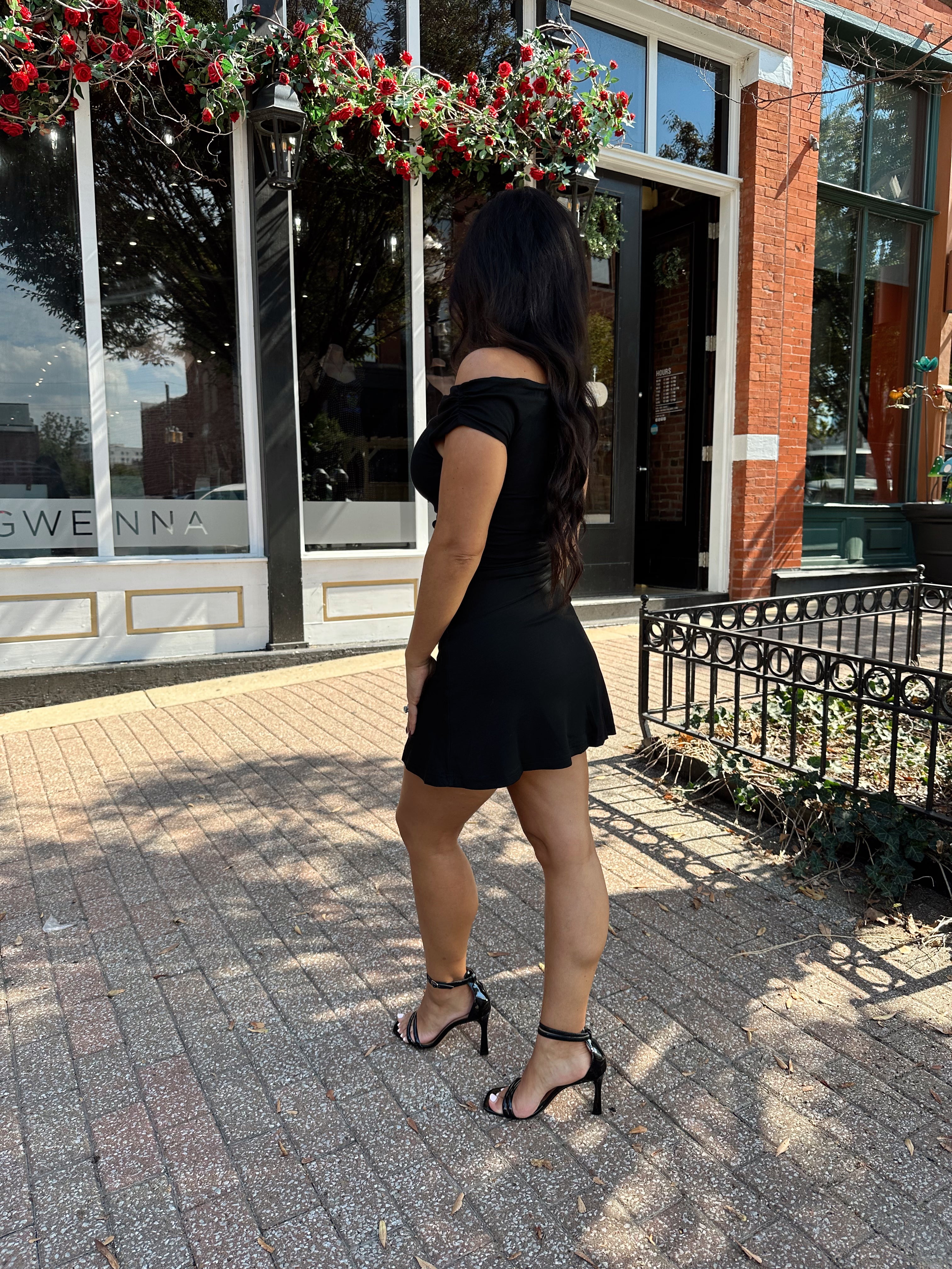 Woman wearing black asymmetrical mini dress with black heels.