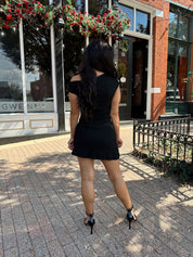 Woman wearing black asymmetrical mini dress with black heels.
