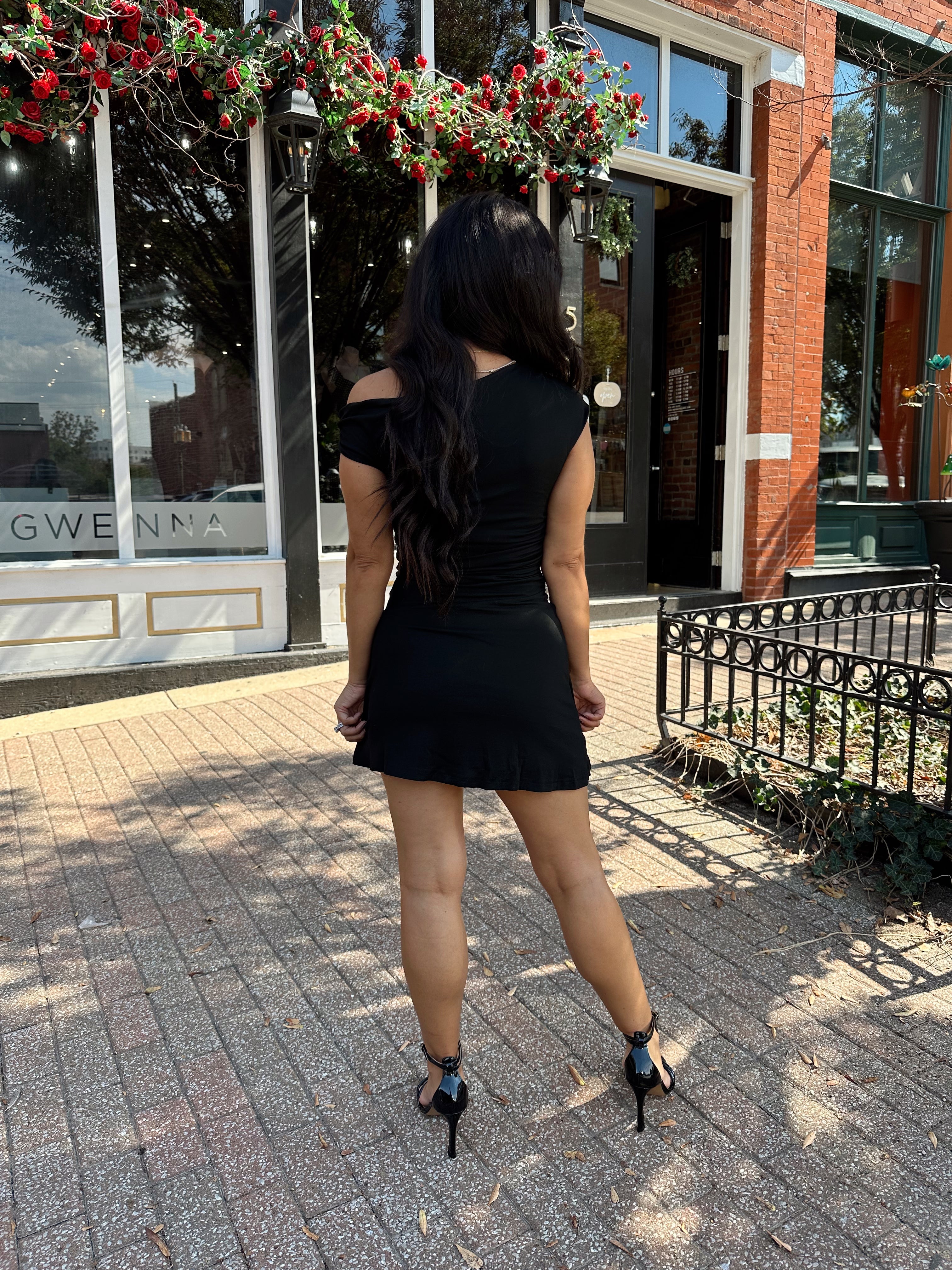 Woman wearing black asymmetrical mini dress with black heels.