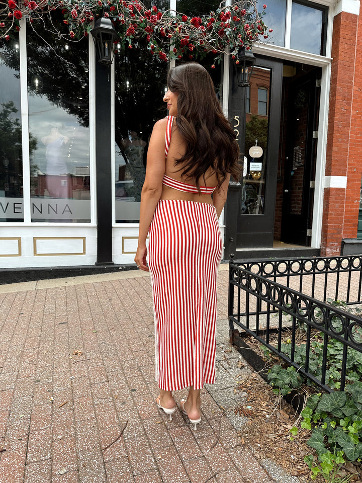 Woman wearing red and white striped textured midi dress with an open back. 