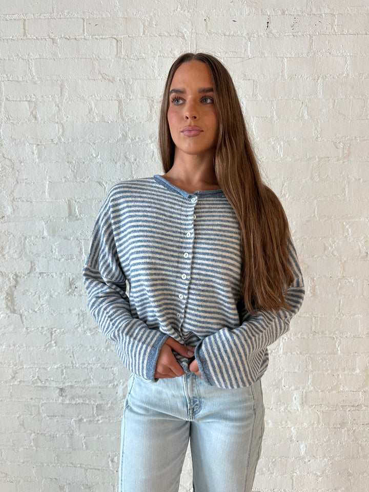 Woman wearing a blue knit striped button down cardigan with light wash barrel jeans. 