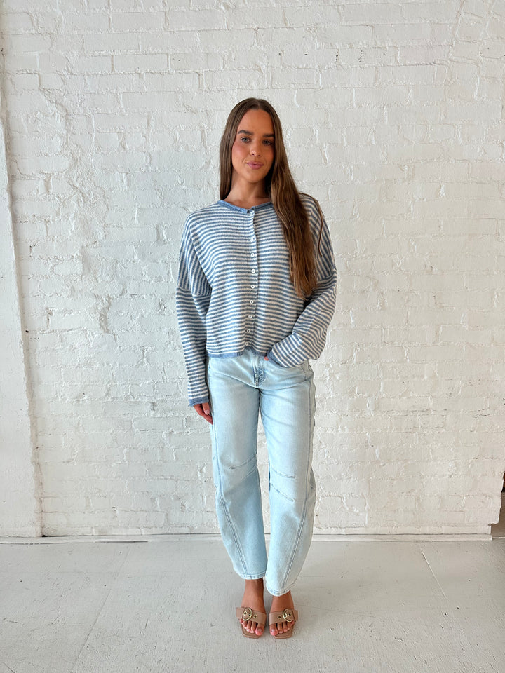 Woman wearing a blue knit striped button down cardigan with light wash barrel jeans. 