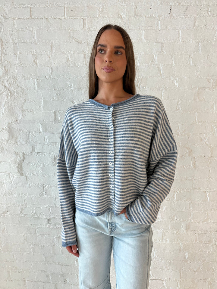 Woman wearing a blue knit striped button down cardigan with light wash barrel jeans. 
