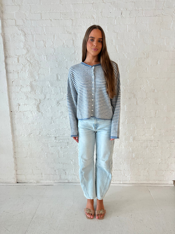 Woman wearing a blue knit striped button down cardigan with light wash barrel jeans. 