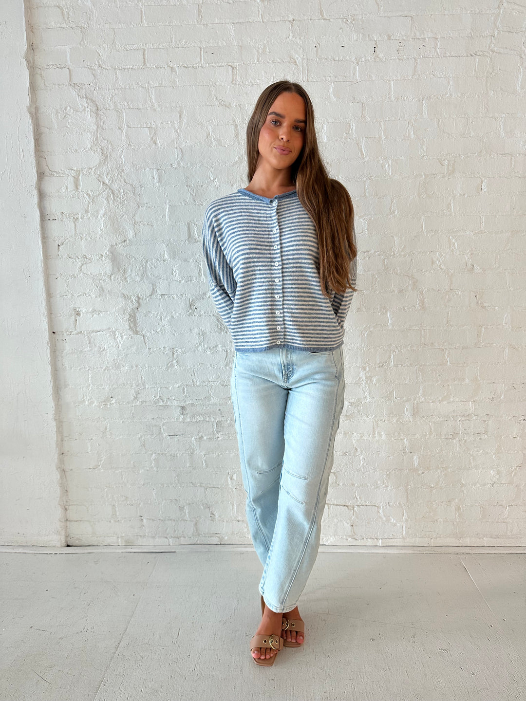 Woman wearing a blue knit striped button down cardigan with light wash barrel jeans. 