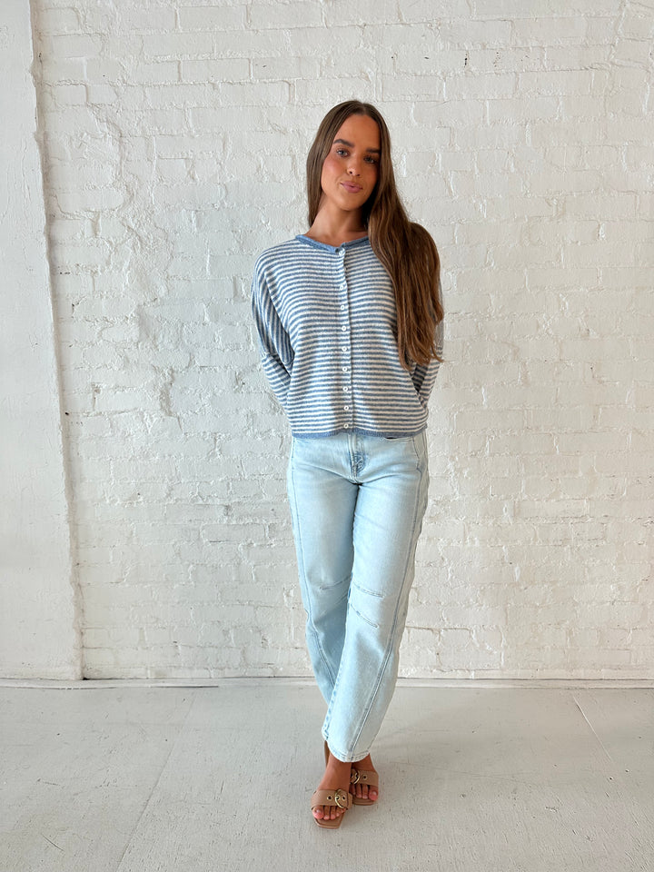 Woman wearing a blue knit striped button down cardigan with light wash barrel jeans. 