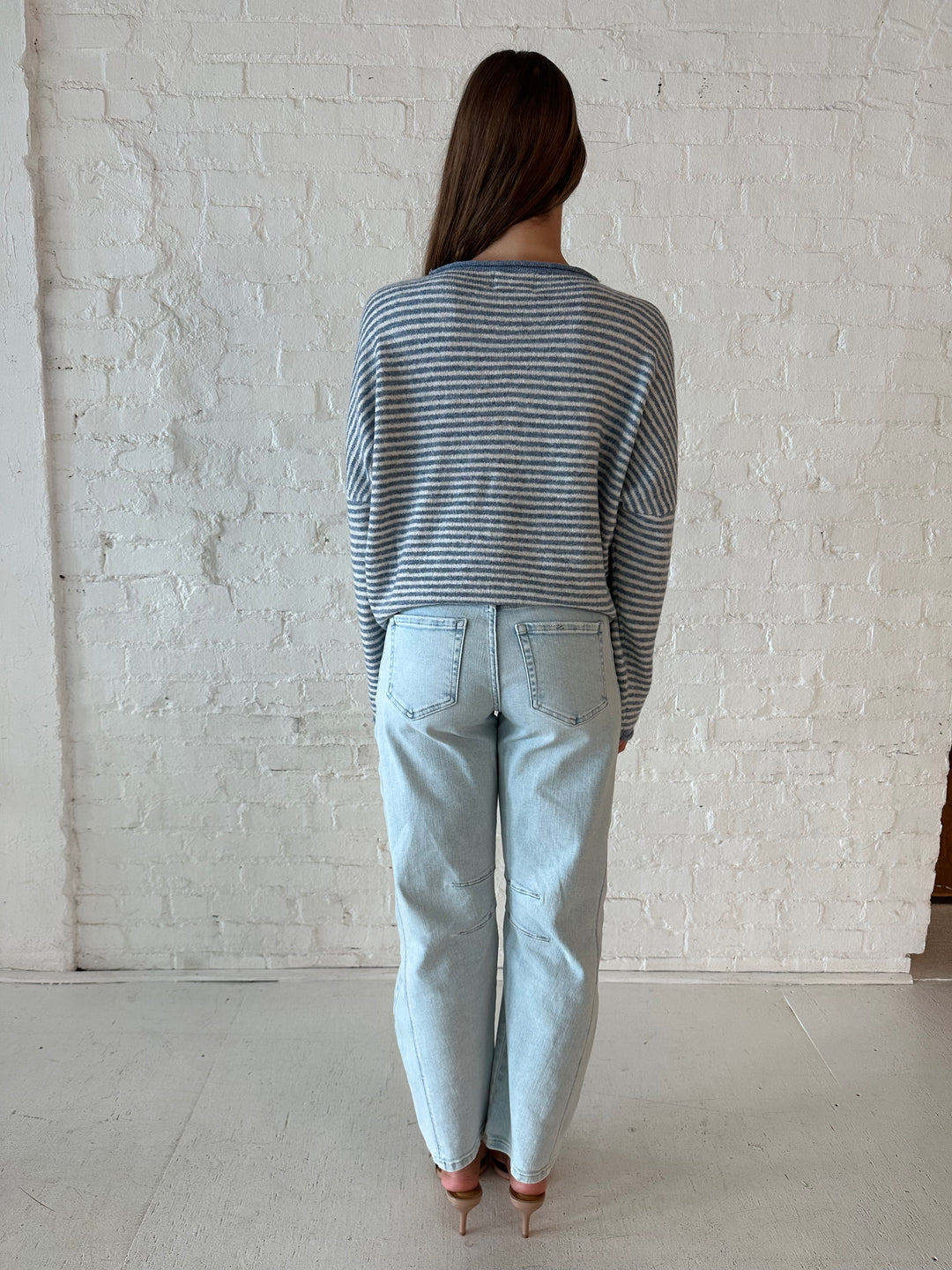 Woman wearing a blue knit striped button down cardigan with light wash barrel jeans. 