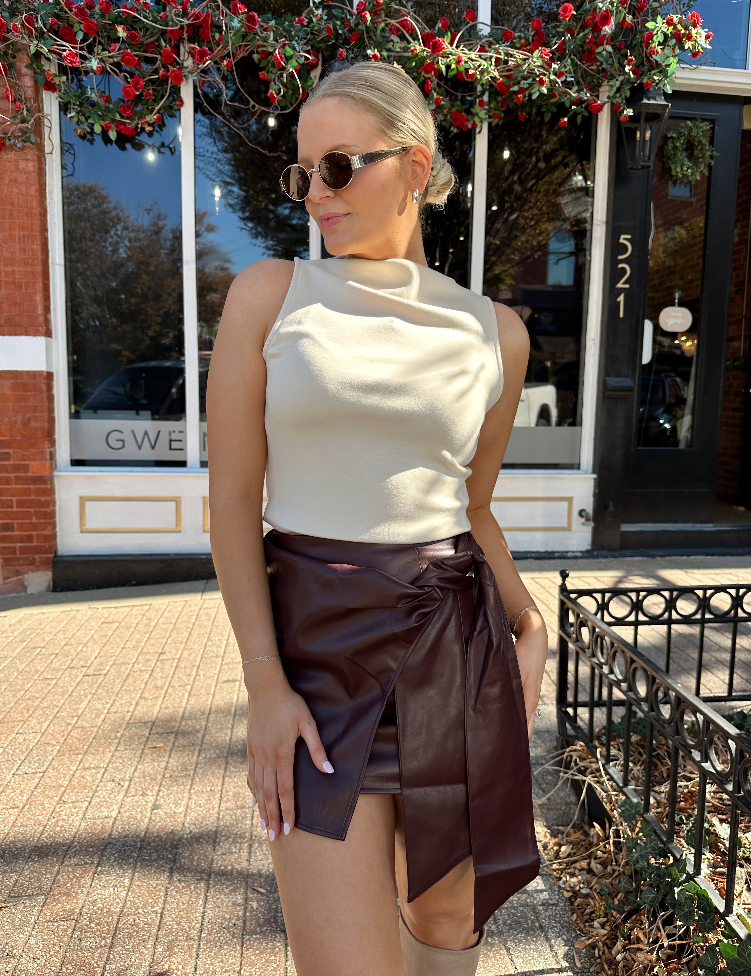 Woman wearing cream sleeveless high neck top and wine leather skort. 