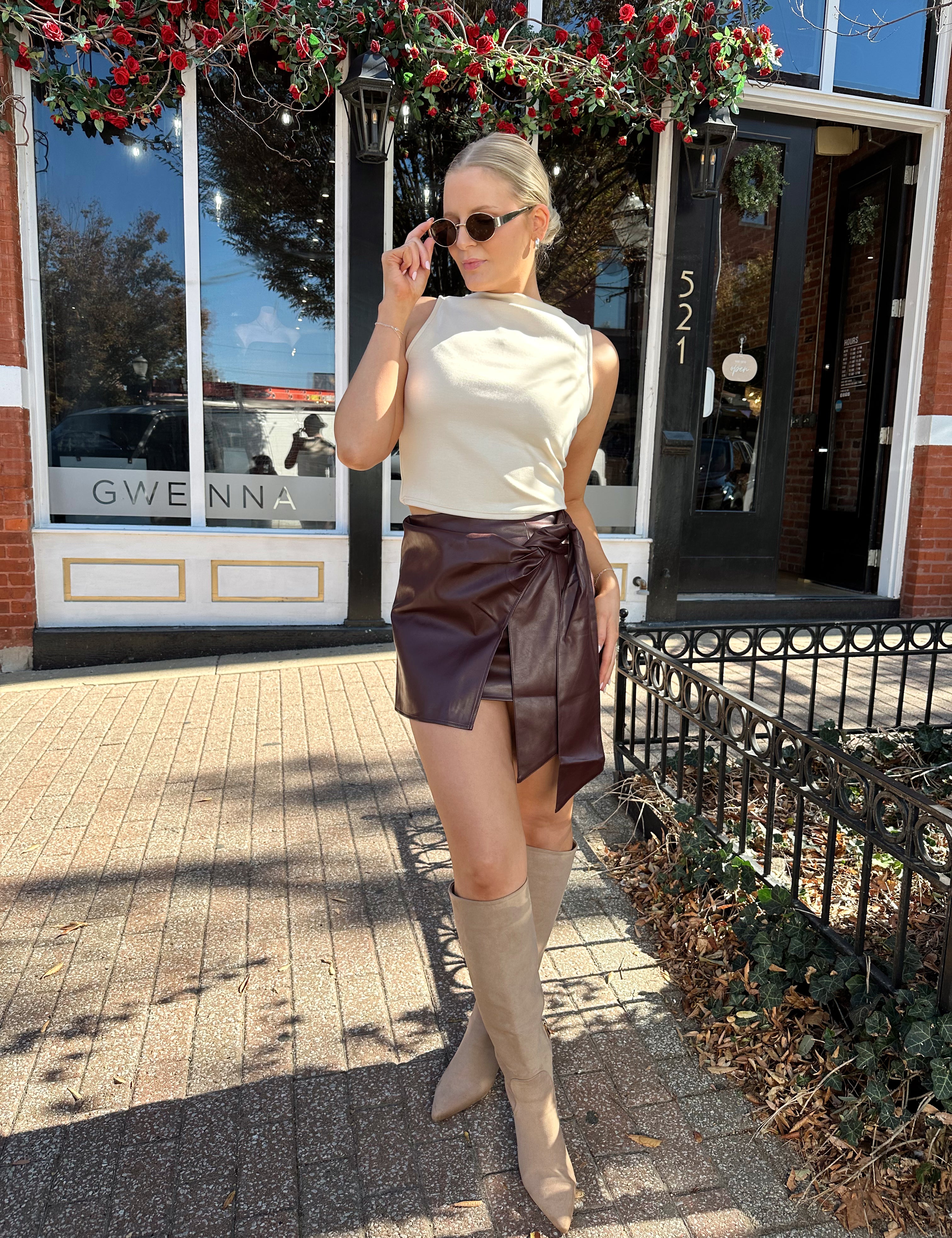 Woman wearing cream sleeveless high neck top and wine leather skort. 