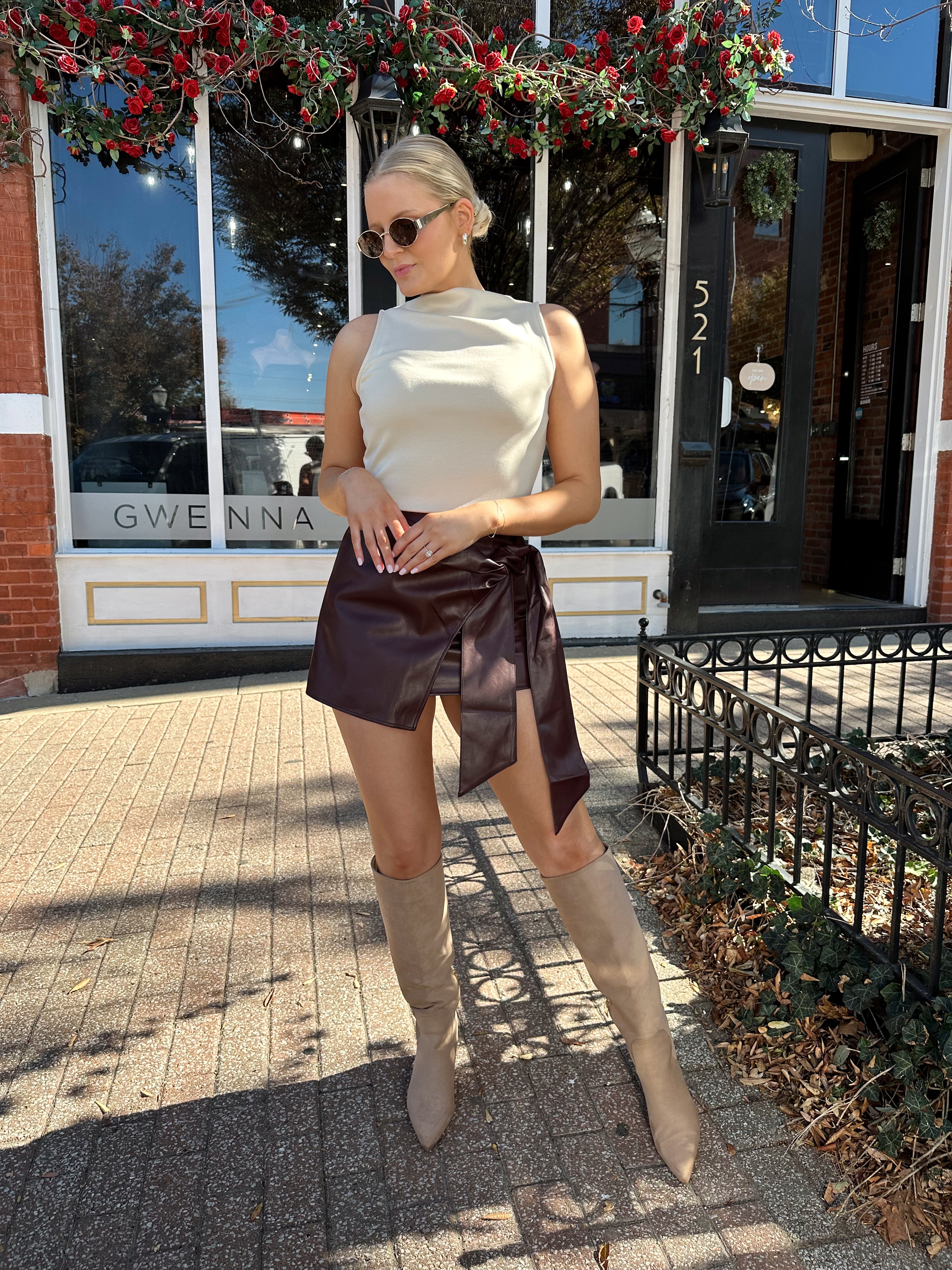Woman wearing cream sleeveless high neck top and wine leather skort. 