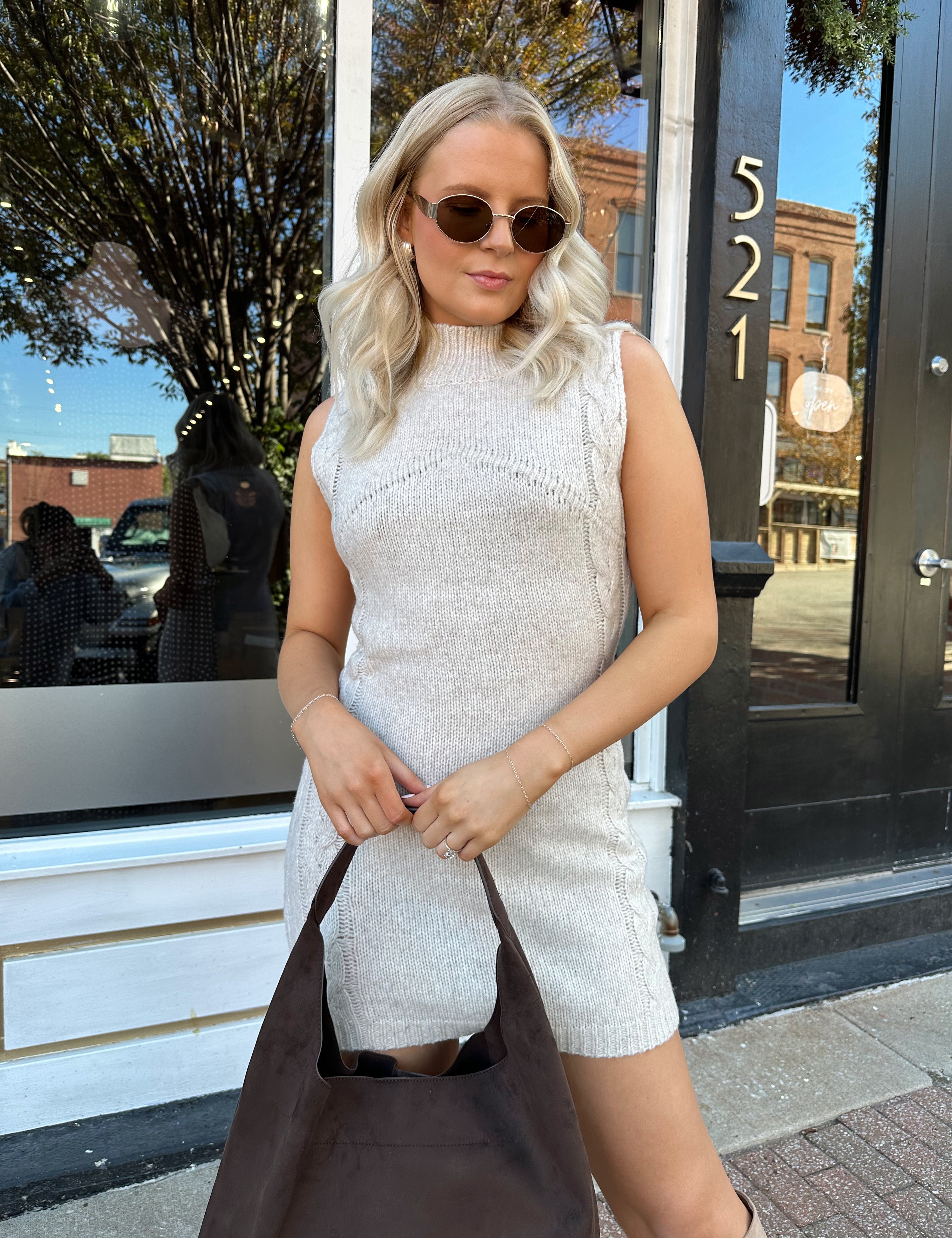 Woman wearing oatmeal colored sleeveless sweater dress with suede knee boots.
