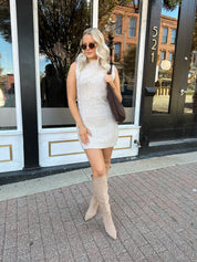 Woman wearing oatmeal colored sleeveless sweater dress with suede knee boots.