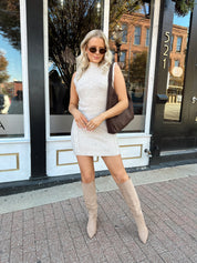 Woman wearing oatmeal colored sleeveless sweater dress with suede knee boots.