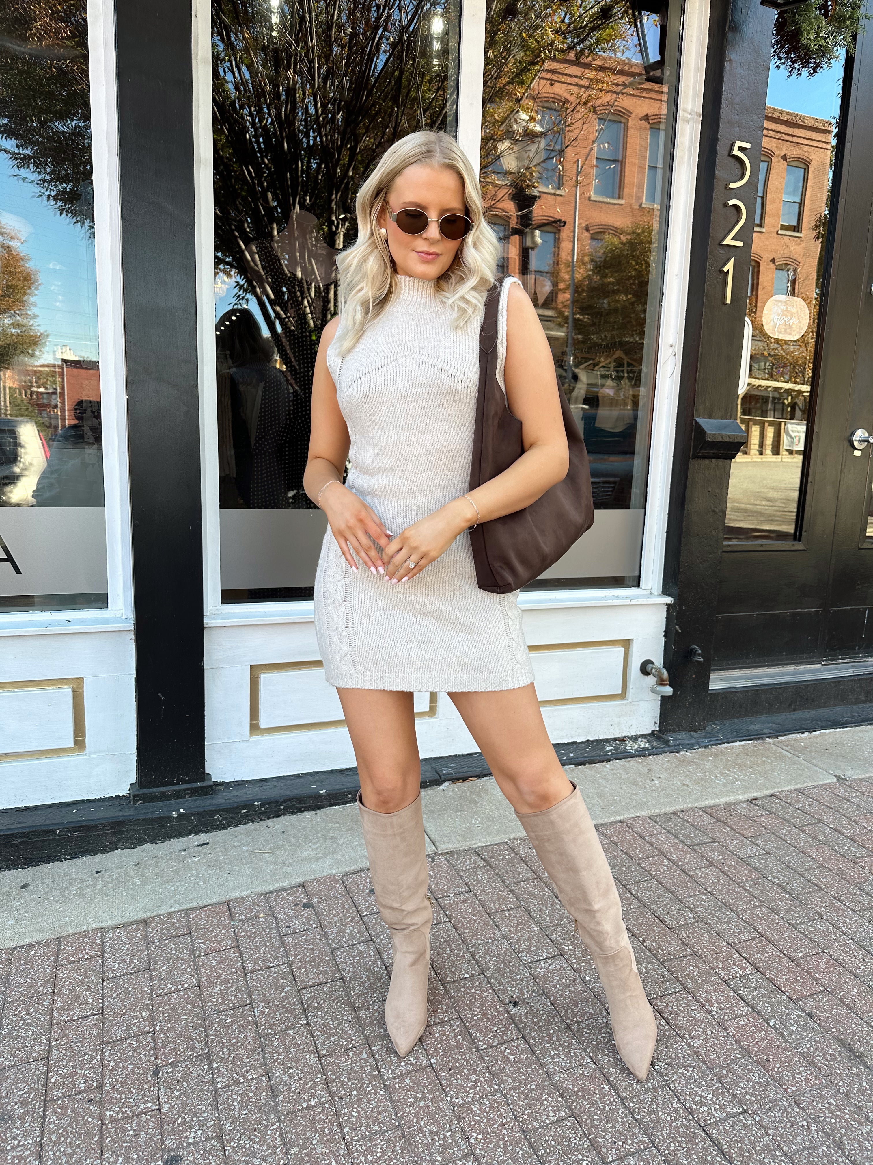 Woman wearing oatmeal colored sleeveless sweater dress with suede knee boots.