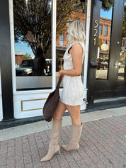 Woman wearing oatmeal colored sleeveless sweater dress with suede knee boots.