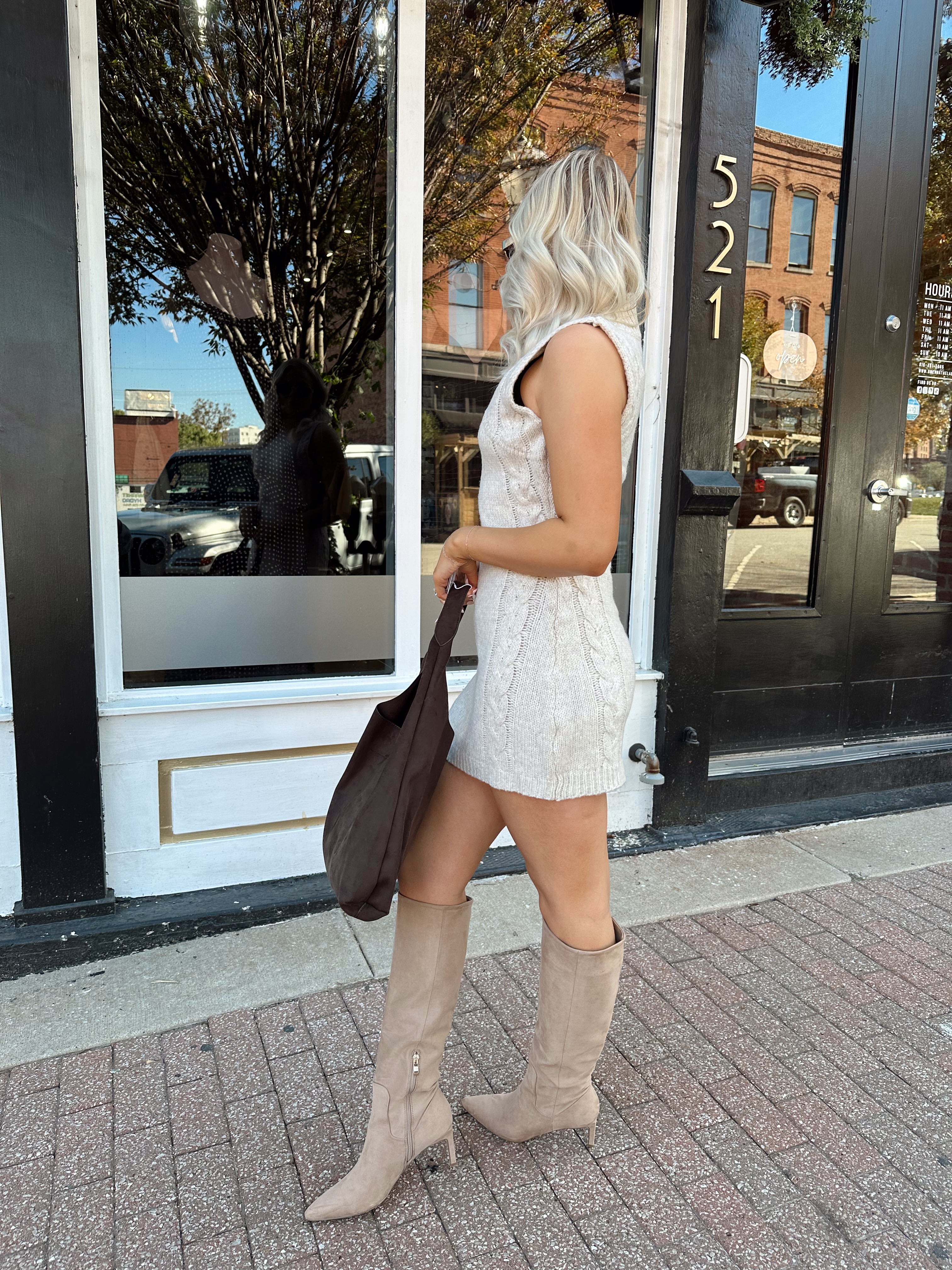 Woman wearing oatmeal colored sleeveless sweater dress with suede knee boots.
