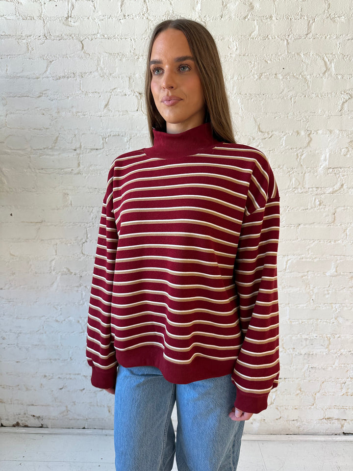 Woman wearing burgundy striped mock neck sweatshirt with medium wash jeans.