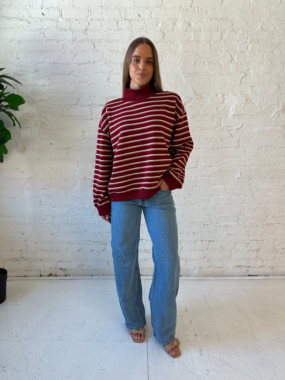Woman wearing burgundy striped mock neck sweatshirt with medium wash jeans.