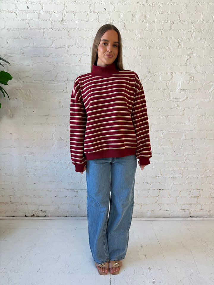 Woman wearing burgundy striped mock neck sweatshirt with medium wash jeans.