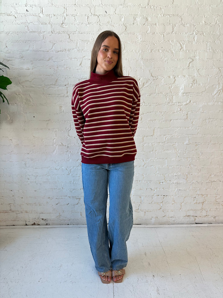 Woman wearing burgundy striped mock neck sweatshirt with medium wash jeans.
