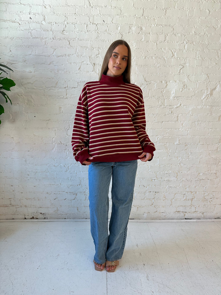 Woman wearing burgundy striped mock neck sweatshirt with medium wash jeans.