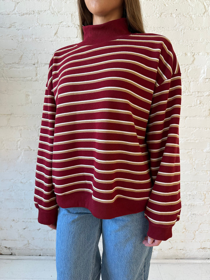 Woman wearing burgundy striped mock neck sweatshirt with medium wash jeans.