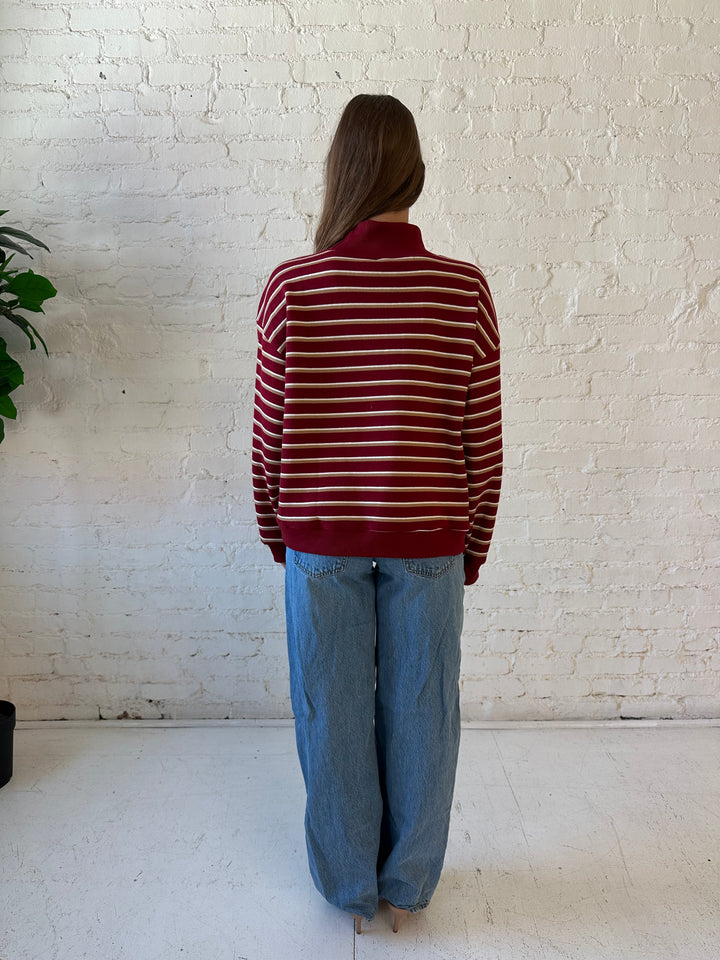 Woman wearing burgundy striped mock neck sweatshirt with medium wash jeans.