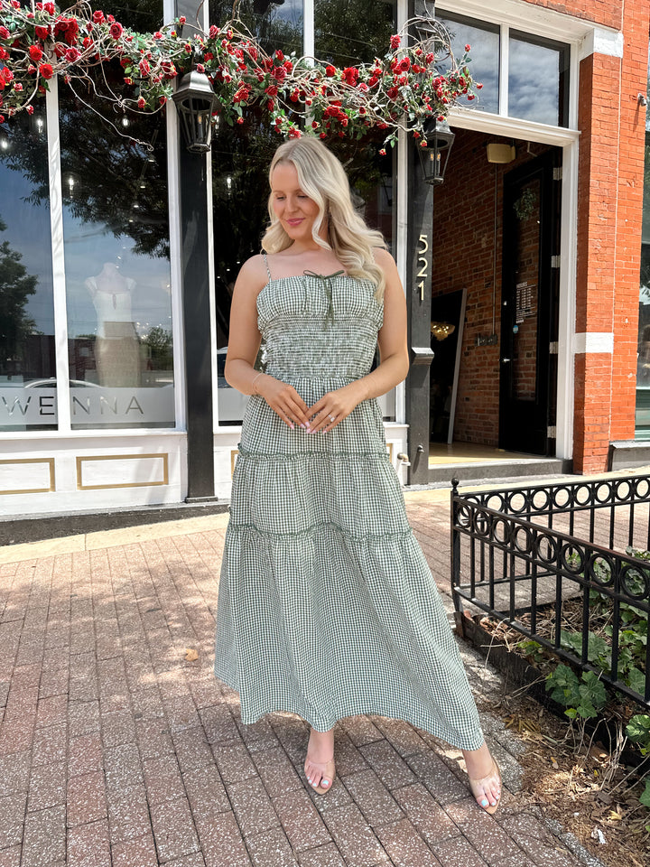 Woman wearing green gingham maxi dress with smocked midsection and adjustable straps.