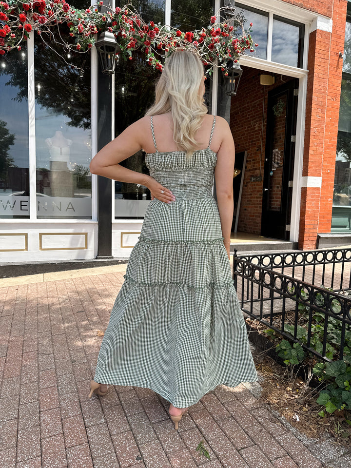 Woman wearing green gingham maxi dress with smocked midsection and adjustable straps.