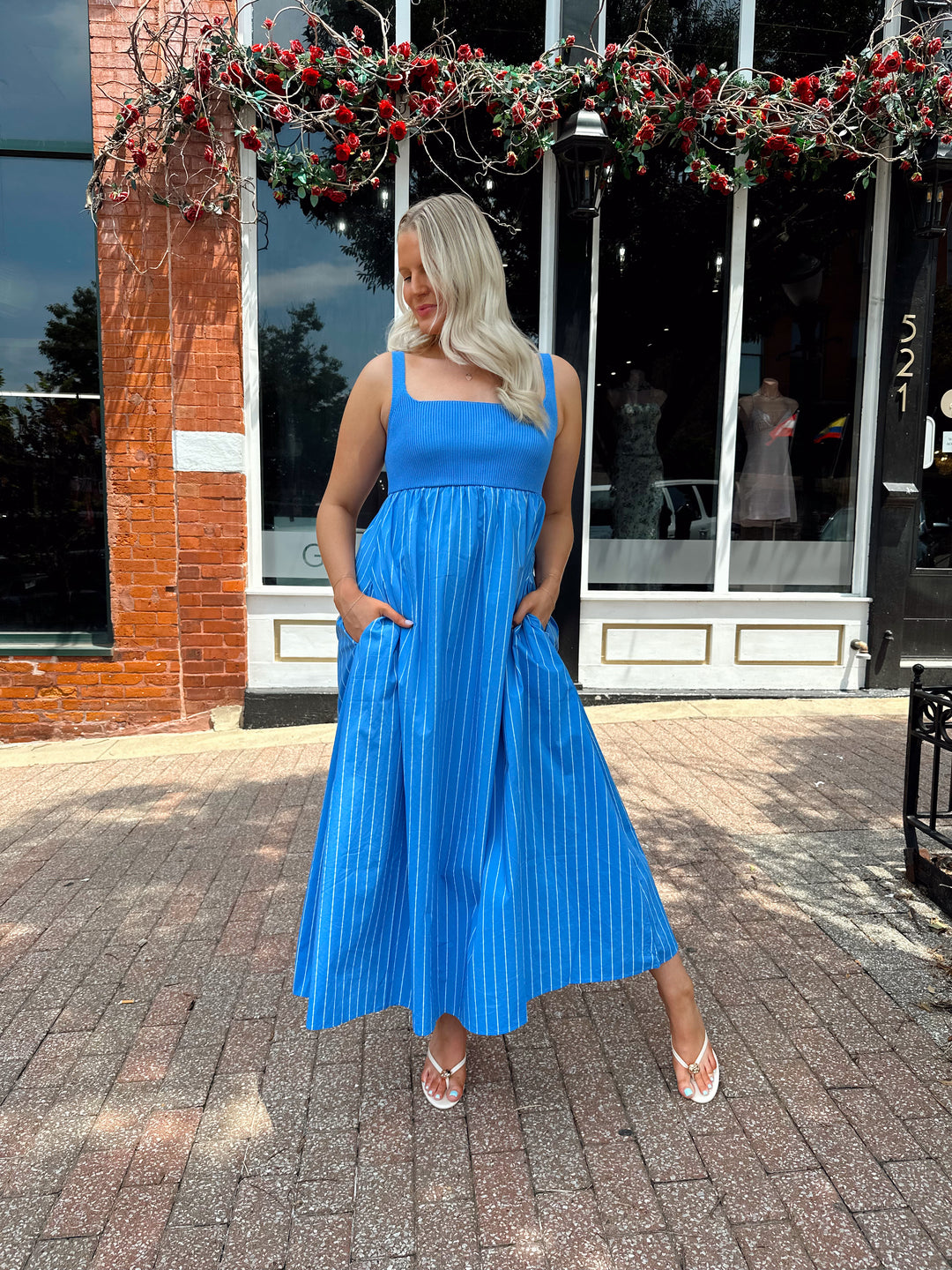 Woman wearing blue striped midi dress with knit bodice, and tie back detail. Has Functional pockets.