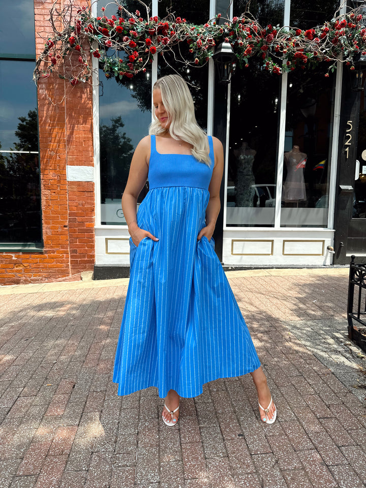 Woman wearing blue striped midi dress with knit bodice, and tie back detail. Has Functional pockets.