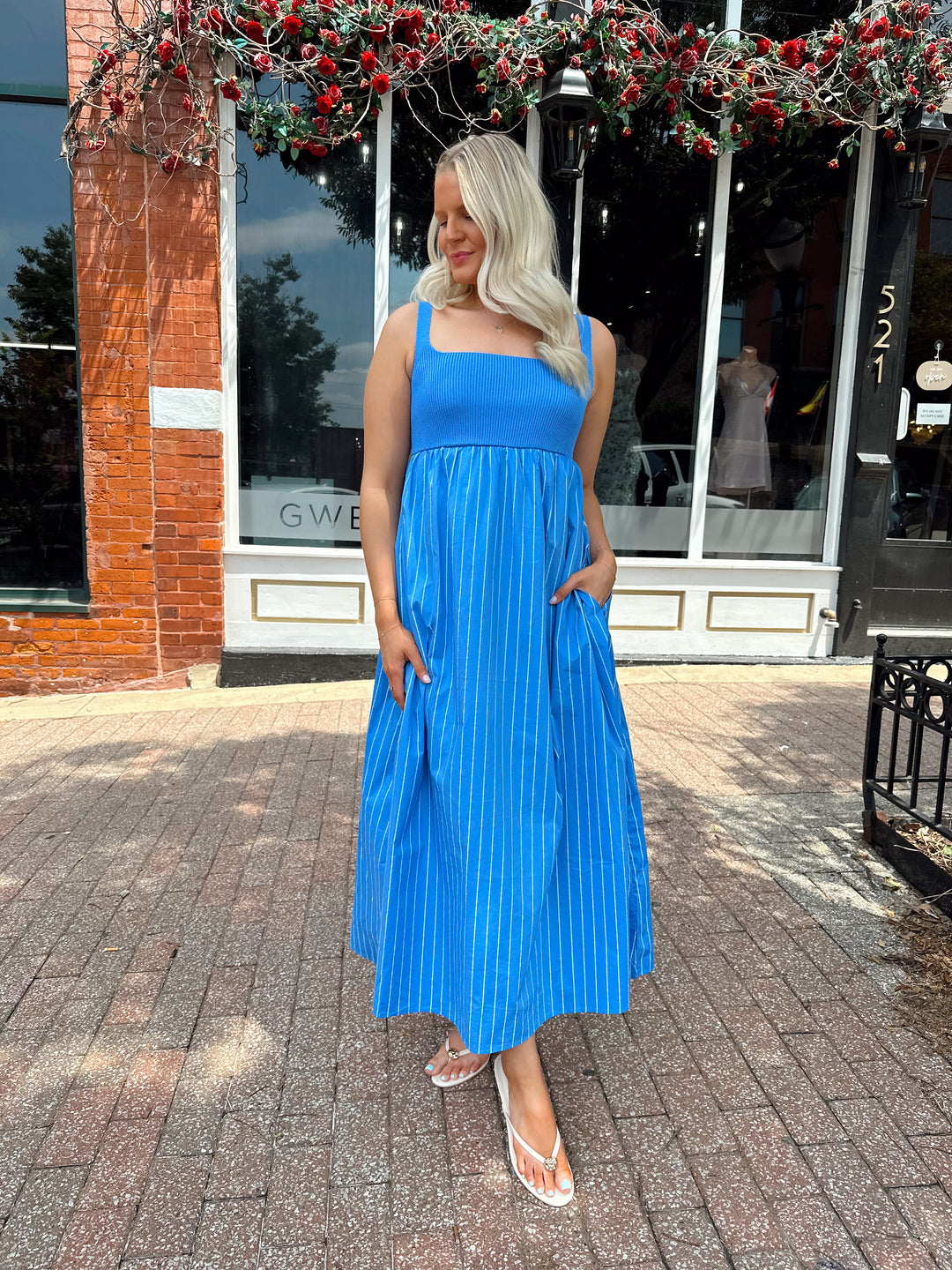 Woman wearing blue striped midi dress with knit bodice, and tie back detail. Has Functional pockets.