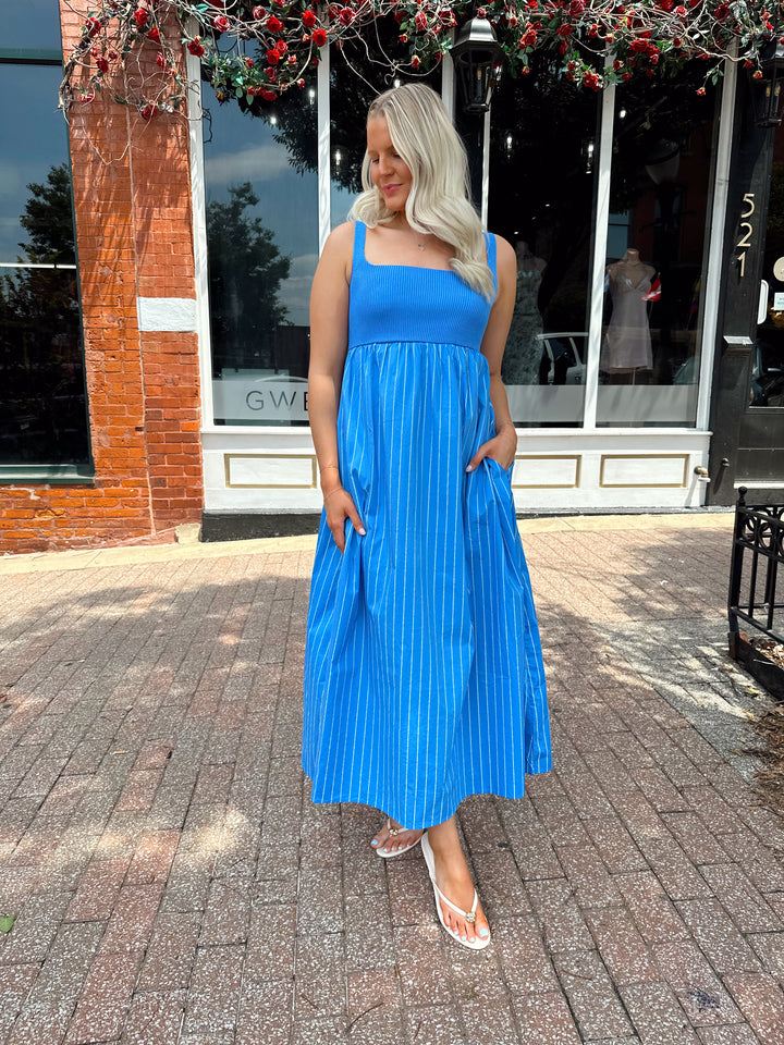 Woman wearing blue striped midi dress with knit bodice, and tie back detail. Has Functional pockets.