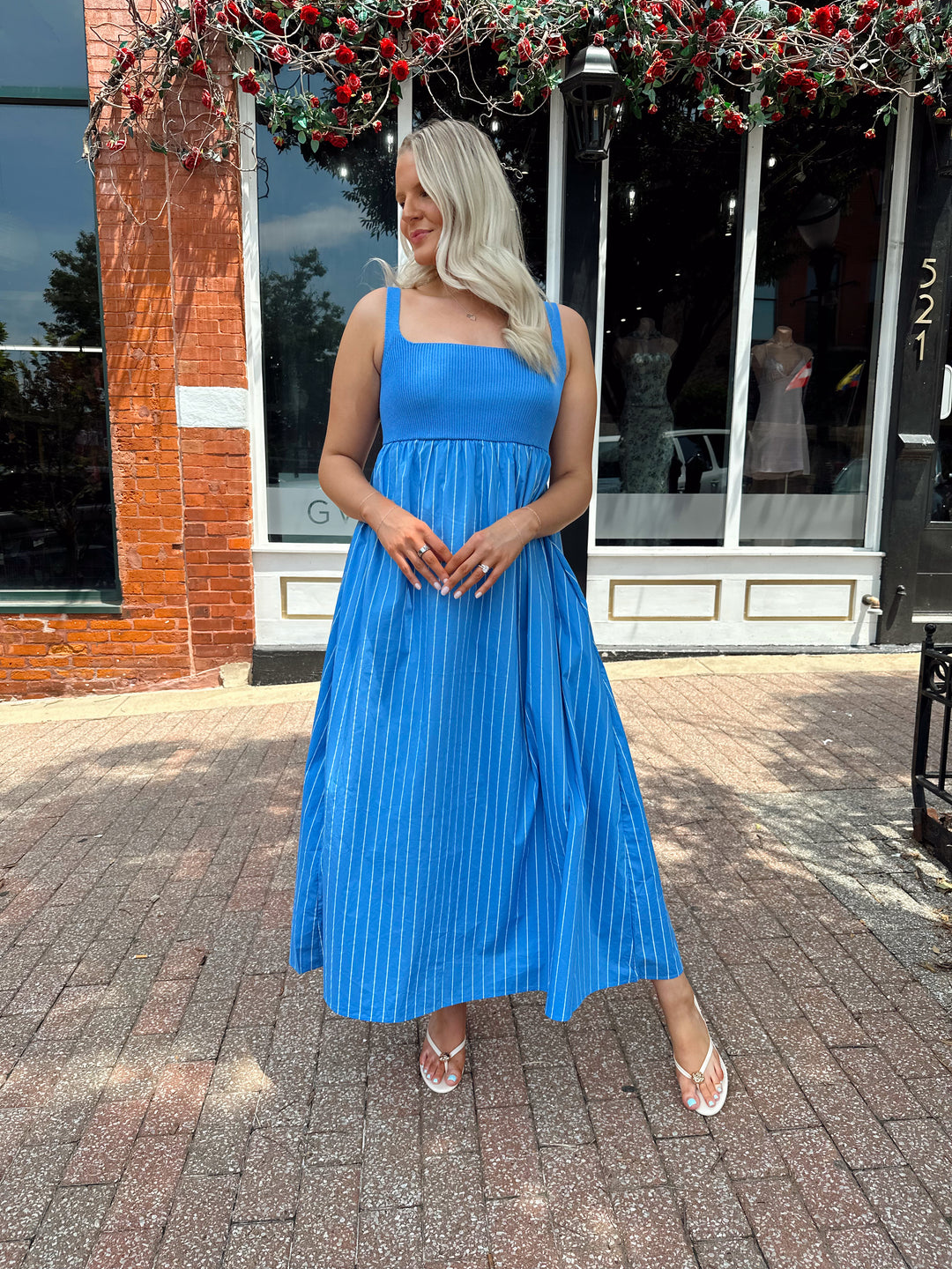 Woman wearing blue striped midi dress with knit bodice, and tie back detail. Has Functional pockets.
