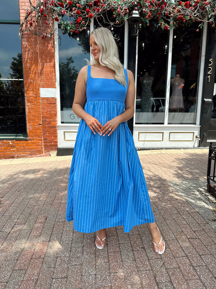 Woman wearing blue striped midi dress with knit bodice, and tie back detail. Has Functional pockets.