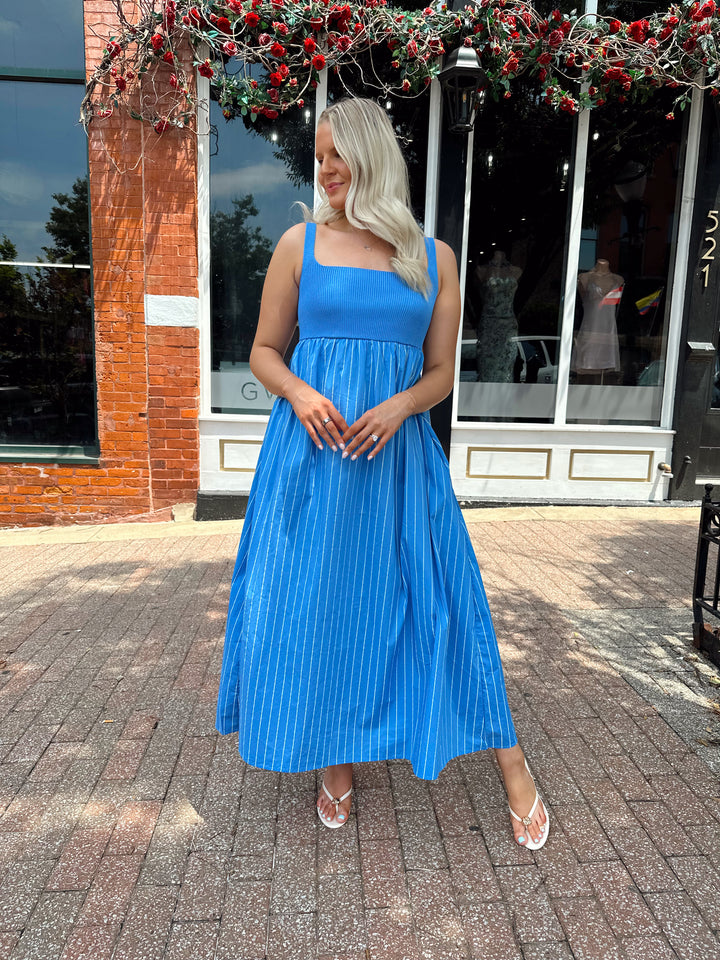 Woman wearing blue striped midi dress with knit bodice, and tie back detail. Has Functional pockets.