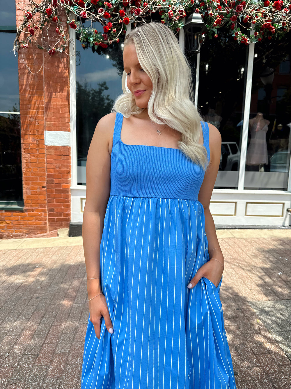 Woman wearing blue striped midi dress with knit bodice, and tie back detail. Has Functional pockets.