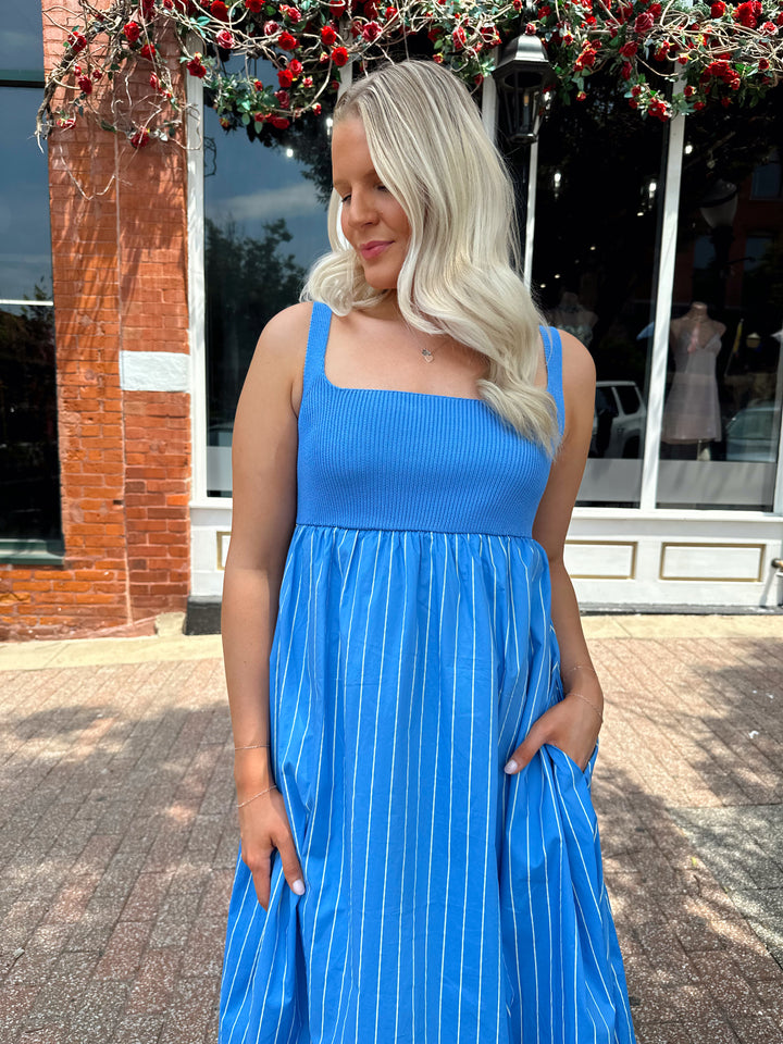 Woman wearing blue striped midi dress with knit bodice, and tie back detail. Has Functional pockets.